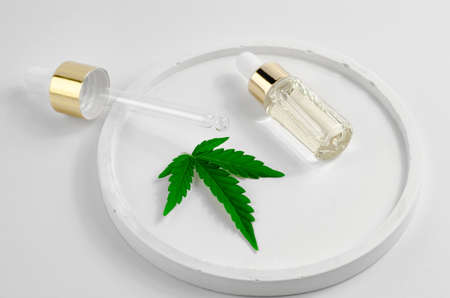 A bottle of hemp oil, a hemp leaf and a dropper on a white saucer. Natural hemp cosmetics. Cosmetics CBD oilの写真素材