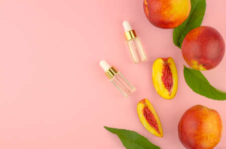 Natural cosmetics, hair care. Natural peach oil. Two bottles with essential peach oil, peaches and green peach leaves on a pink background.の写真素材