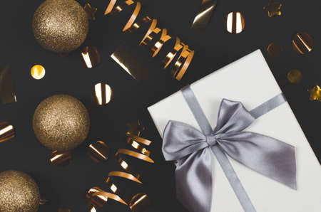 Christmas composition. Large white gift box and gold christmas decor on black background, christmas...