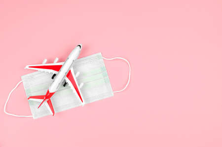 An overhead view of a red and white toy plane and a protective medical mask on a pink background....