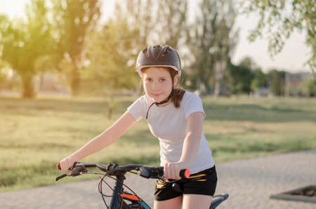 An 11-year-old girl in a protective sports helmet sits on a bicycle. Girl with a bike in the park. Children's sports and a healthy lifestyleの写真素材