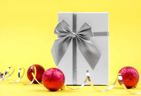 Christmas background. Light gift box, christmas balls and serpentine on a yellow backgroundの写真素材