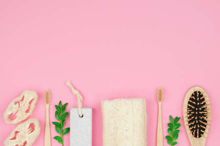 Eco friendly personal care products on a pink background with place for text. Bamboo toothbrushes, a wooden comb and a loofah washcloth with green leaves.の写真素材