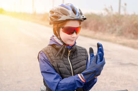 Girl cyclist puts on sports gloves. Teenage girl in protective bicycle helmet, glasses and glovesの写真素材