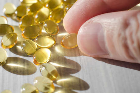 Close-up of a male hand takes vitamin D 3 capsules on a white wooden table