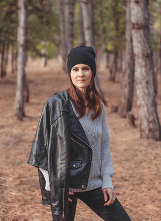 Photo of a young woman in a leather jacket and a black hat in the forest. Portrait of a beautiful...