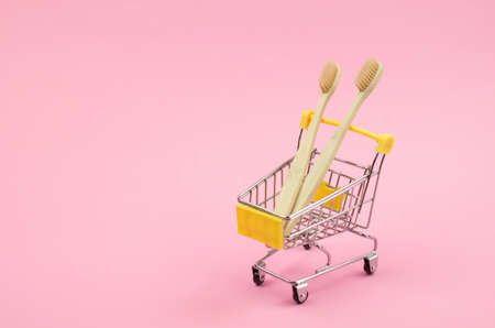 Two wooden toothbrushes in a shopping trolley on a yellow backgroundの写真素材