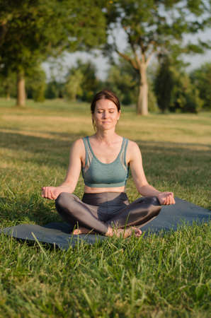 Young woman meditates in the park in the lotus position at sunset. Yoga classes in natureの写真素材