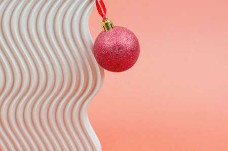Red Christmas ball on a wavy geometric shape. Minimalistic christmas background with place for textの写真素材