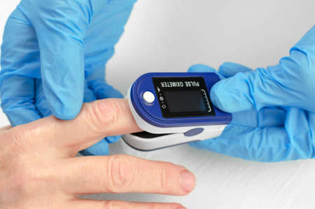 Measurement of saturation in a 60-year-old woman. The hands of a doctor in medical gloves apply a...