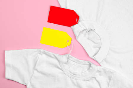 Two white T-shirts on a pink background with blank price tags. Blank label on clothesの写真素材