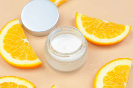 Moisturizing cream with orange extract. Open jar of cream and orange slices on beige backgroundの写真素材