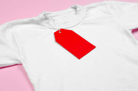 Blank red price tag on white t-shirt. White t-shirt on a pink background with a red blank label.の写真素材