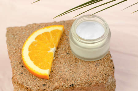 Open jar of moisturizer and orange slice on natural stone background. Moisturizing cream with orange...