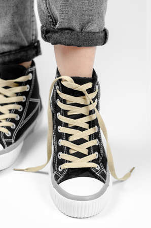 Sneaker with untied laces on a female leg on a white background