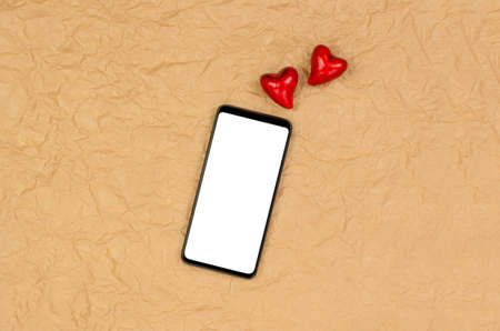 Smartphone with a blank white display on a crumpled beige background with hearts.の写真素材