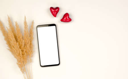 Smartphone with a blank white display on a beige background with hearts and pampas grass.の写真素材