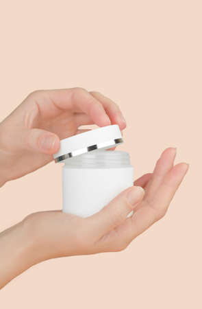 Female hand holds a jar of moisturizer on a pink background, mockup. A woman opens a jar of skin moisturizer. skincare concept.の写真素材