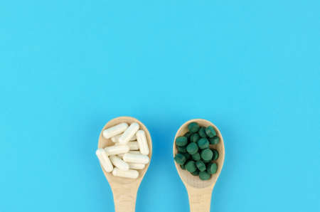 White and green pills in wooden spoons on a blue backgroundの写真素材