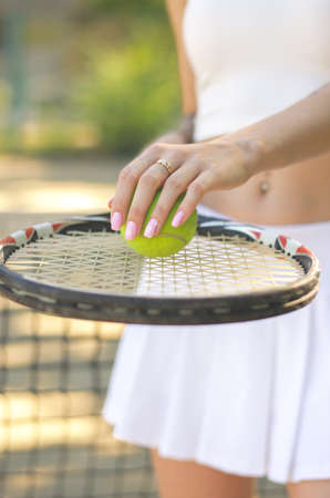 Ball on a tennis racket. Sportswoman holding tennis racket and ball in her hands