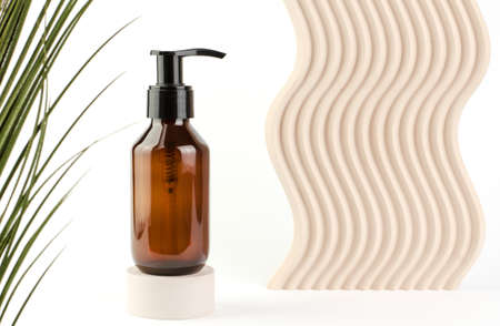 Brown cosmetic bottle with a dispenser on a podium on a white background. Care cosmetics for face and body. Moisturizing body lotion, body milk, shower gel.の写真素材