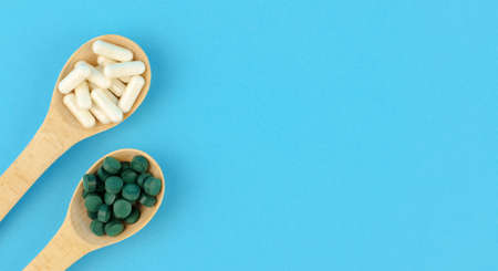 White and green pills in wooden spoons on a blue backgroundの写真素材