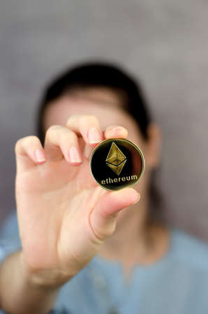 Ethereum coin in a female hand close-up. Unrecognizable woman holding ethereum in front of her face. Cryptocurrencyの写真素材