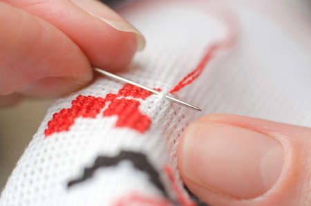 Close-up of female hands cross-stitching on white canvas. A woman embroiders the national symbols of Ukraine with a crossの写真素材