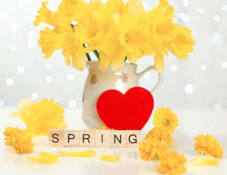Spring word on wooden cubes. spring postcard. Jug with a bouquet of daffodils and a red heart on a...