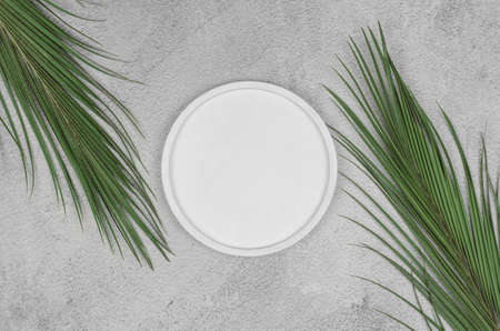 White round podium on a light gray background with palm branches on the sides. Space for product...