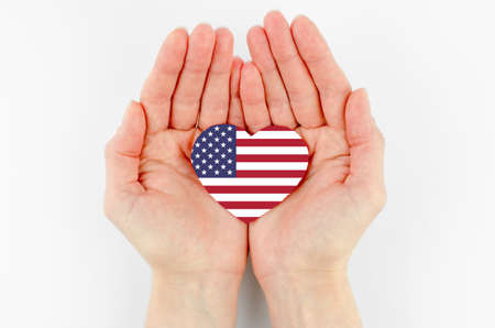 US flag in the shape of a heart in female palms on a white background.