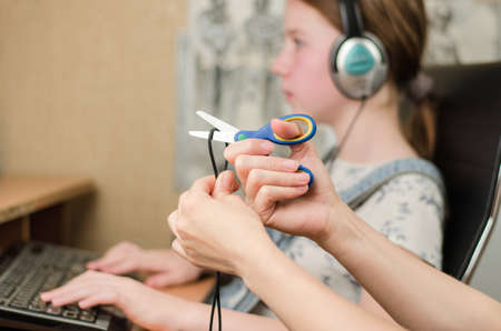 In the foreground, female hands are cutting the headphone cord with scissors, in the background is a...