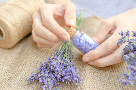 Lavender salt for spa treatments. Lavender sea salt in a small transparent bottle in female hands and fresh lavender flowers.の写真素材