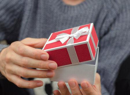 Open gift box in female hands, close-up. Woman opening a small red gift box