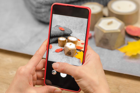 The phone in female hands makes a photo. Women's hands take a photo of candles in golden pots in an...
