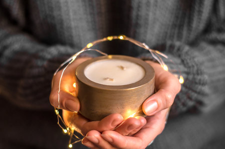 A woman's hand holds a decorative candle in a golden pot and garlands, minimal compositionの写真素材