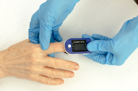 The hands of a doctor in medical gloves apply a pulse oximeter to the finger of an elderly Chinese...