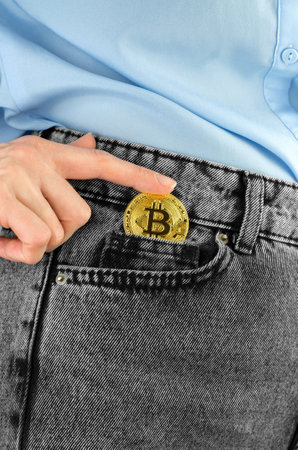 A woman's hand puts a golden bitcoin in a jeans pocket, close-up. world cryptocurrencyの写真素材