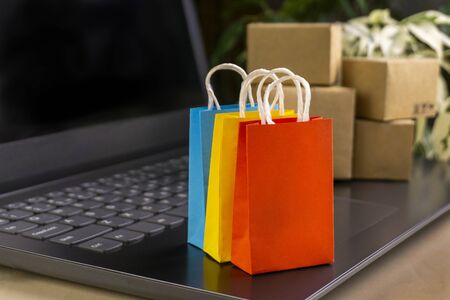 online shopping concept. little shopping cart, boxes, colorful bags, bank card, dollars stand on laptopの写真素材