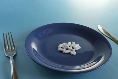 pills on blue plate with knife and fork. diet or medicine conceptの写真素材
