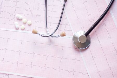 cardiogram with stethoscope, pen, magnifier, pills and glasses lay on a tableの写真素材