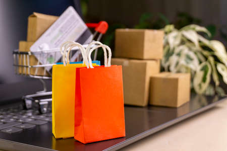 online shopping concept. little deliver boxes, smartphone, shopping bags, shopping bascket stand on laptop. copy spaceの写真素材
