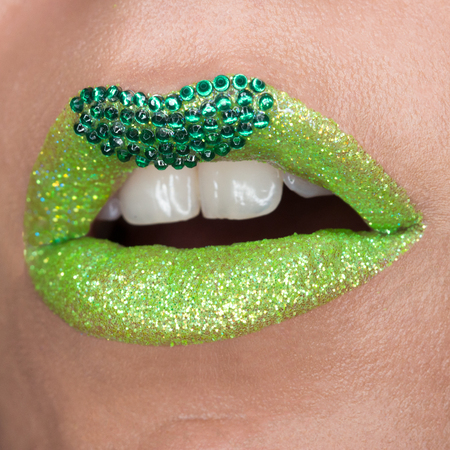 Green lips with sparkles covered with gemstones. Beautiful green lipstick on her lips, white teeth open mouth. Lip artの写真素材