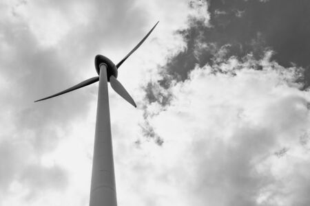 Wind turbine under cloudy sky, black and white bw. View from the ground. Windfarm, wind power plant