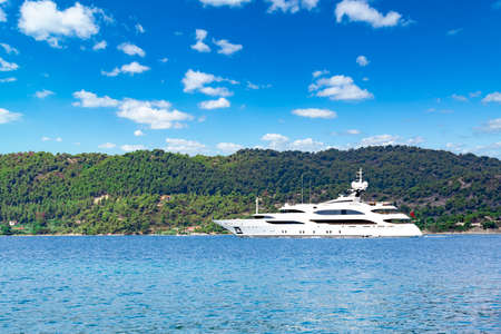 huge motor yacht sailing in the sea near island with green mountains, sunny day with clouds, blue...