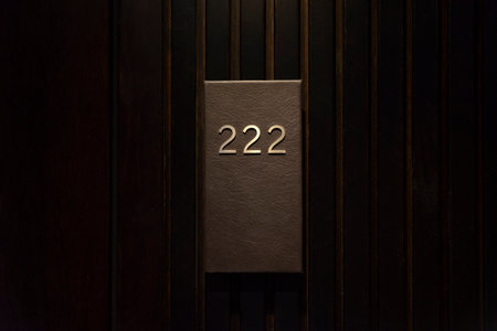 Hotel room with 222 number, dark wood door, black number plate with golder numbers