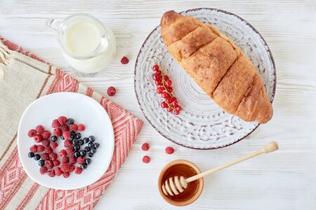Different ingredients for breakfast. Croissants on plate on the wood board, berries, coffee, milk...