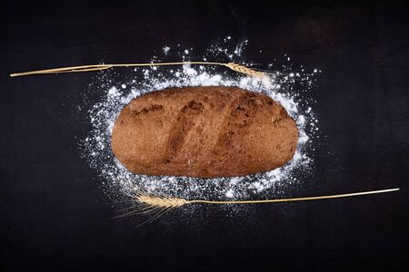 Eliptic form bread on a black background, bread from a stove on dark boards, a dough for a designer,...
