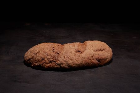 Eliptic form bread on a black background, bread from a stove on dark boards, a dough for a designer,...