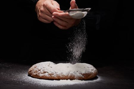 baked oval rye bread in sprinkles of white flour, black backgroundの写真素材
